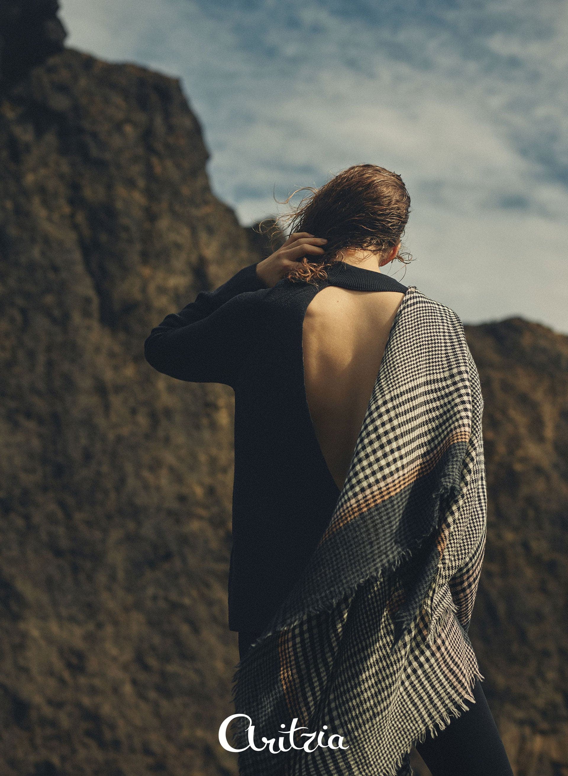 Model in an open-back top with a check scarf against cliffs