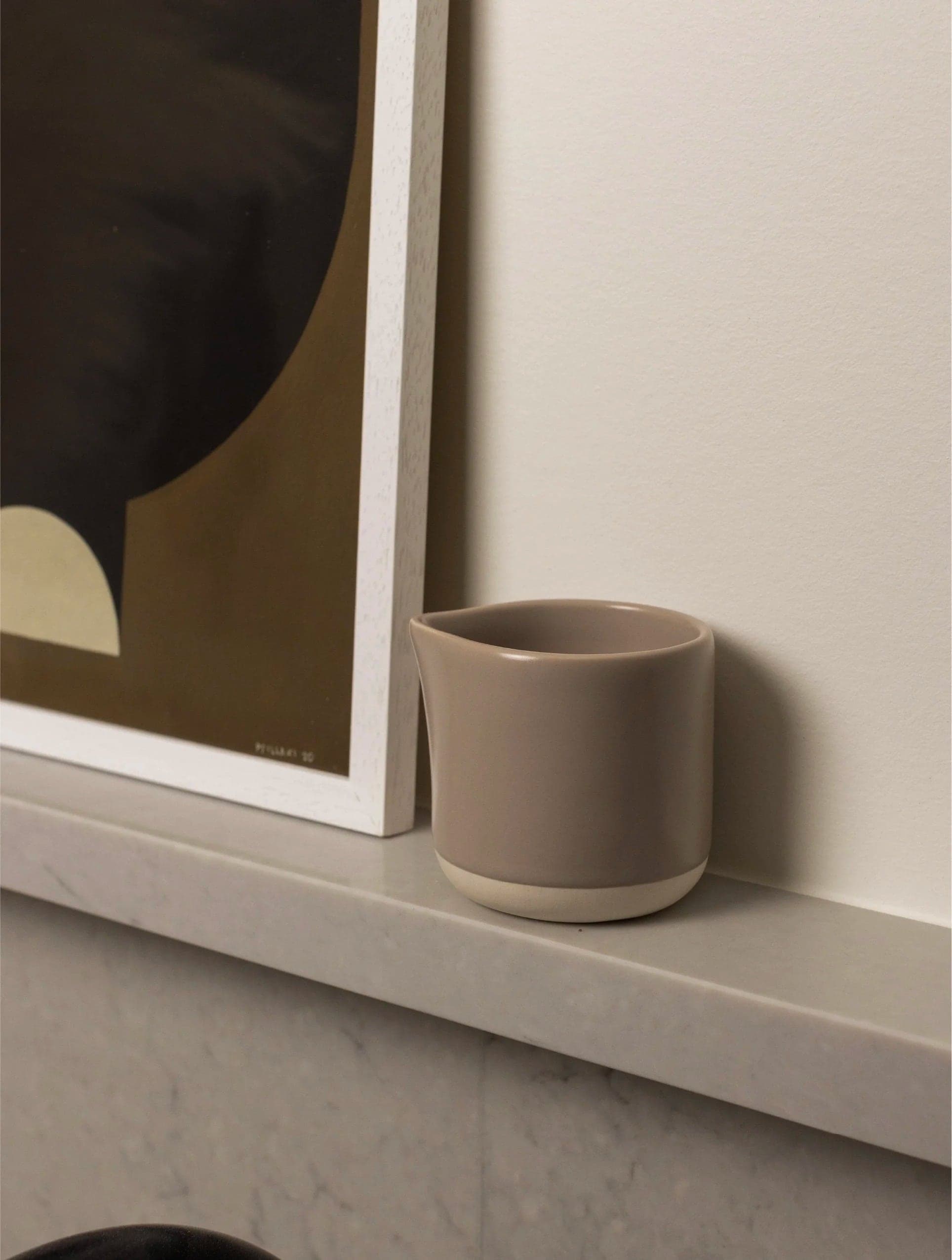 Taupe jug beside a framed print on a stone ledge