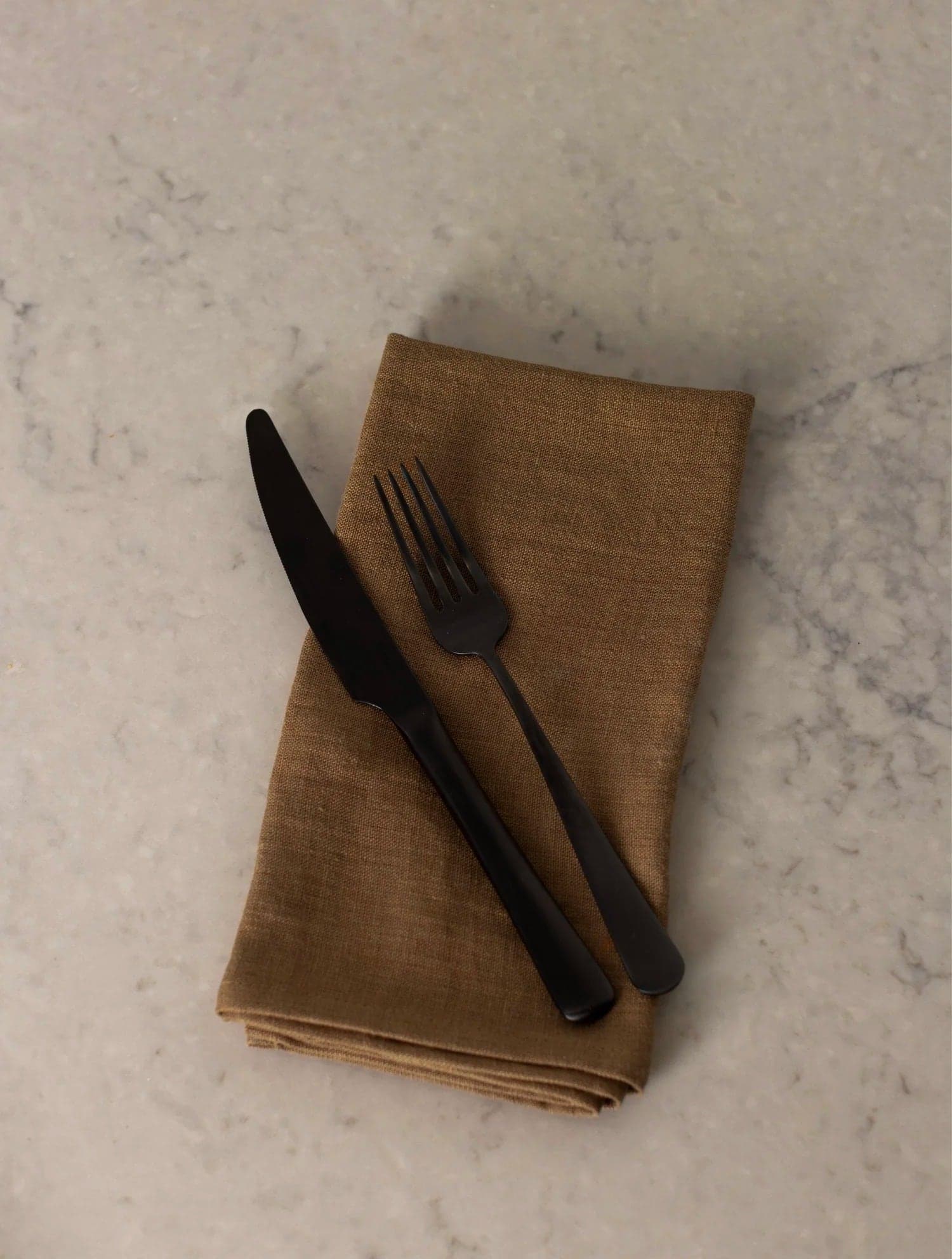 Black cutlery on a linen napkin on marble