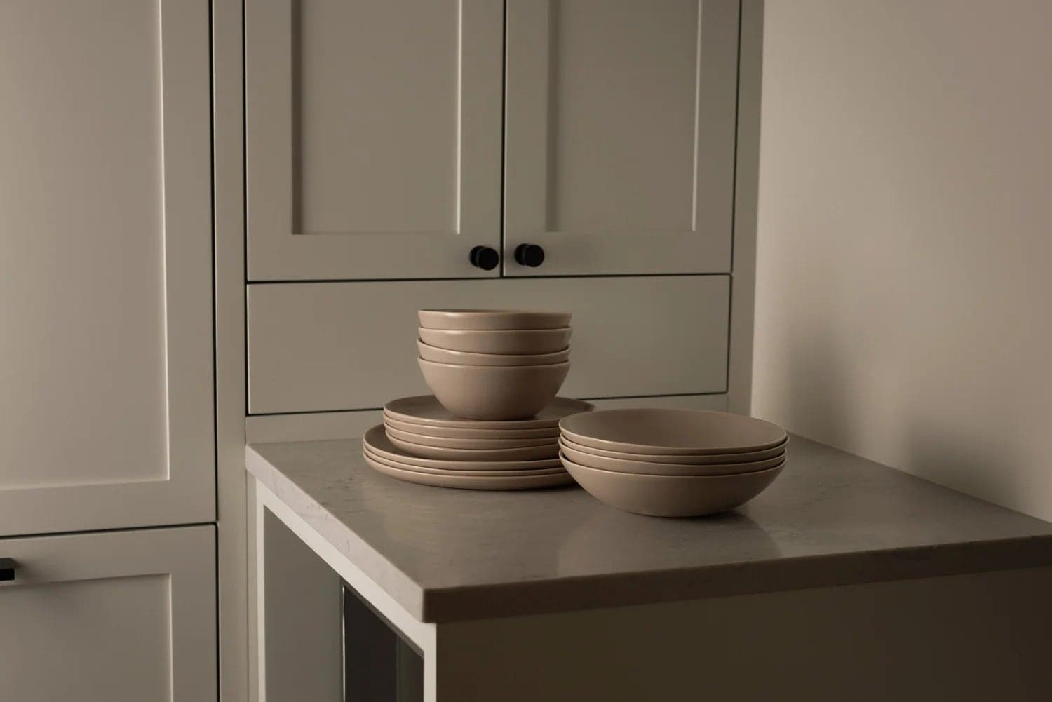 Stacked taupe plates and bowls on a kitchen counter