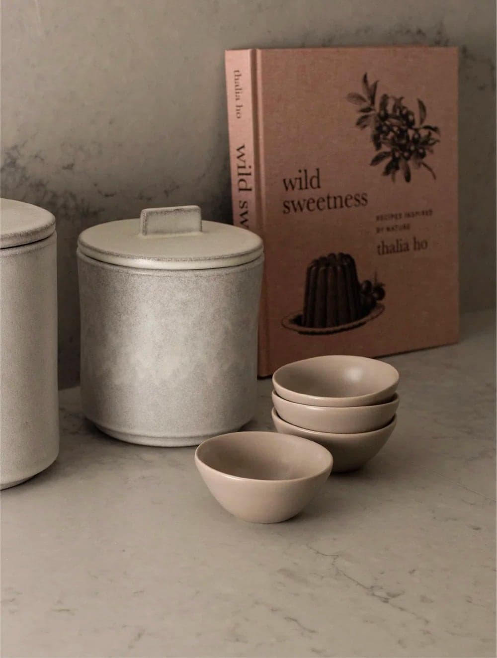 Small taupe bowls beside ceramic canisters and a cookbook