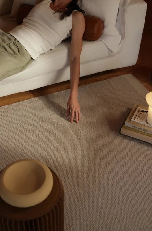 Hand reaching down to a woven rug from the sofa