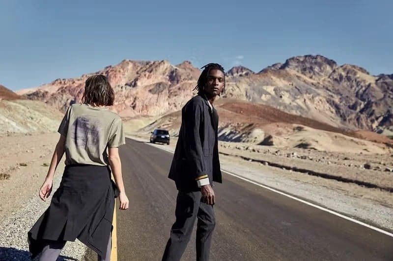 Two models crossing a desert road below painted hills