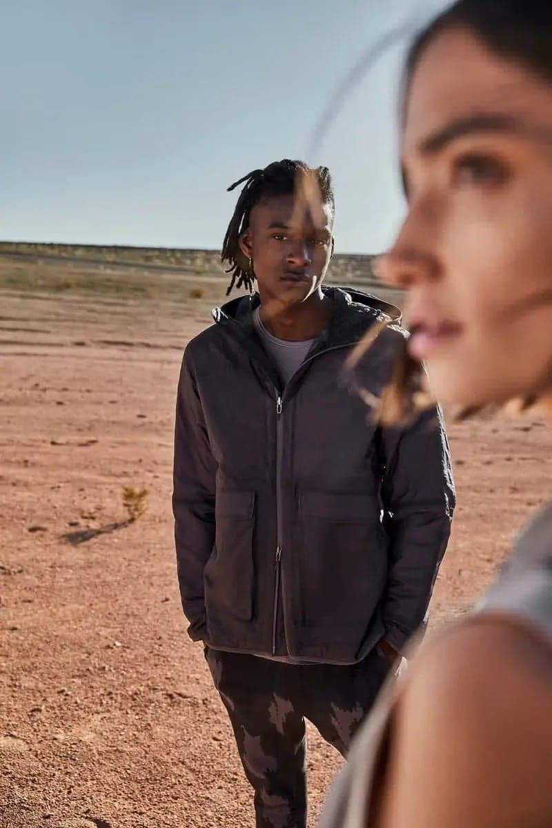 Model in a dark jacket in the desert, another in soft focus