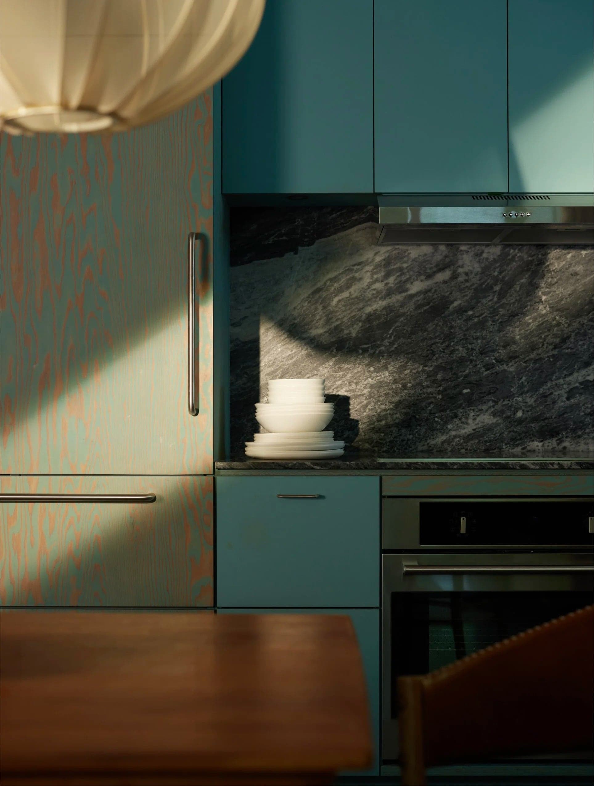 Blue kitchen with a marble backsplash under a paper pendant