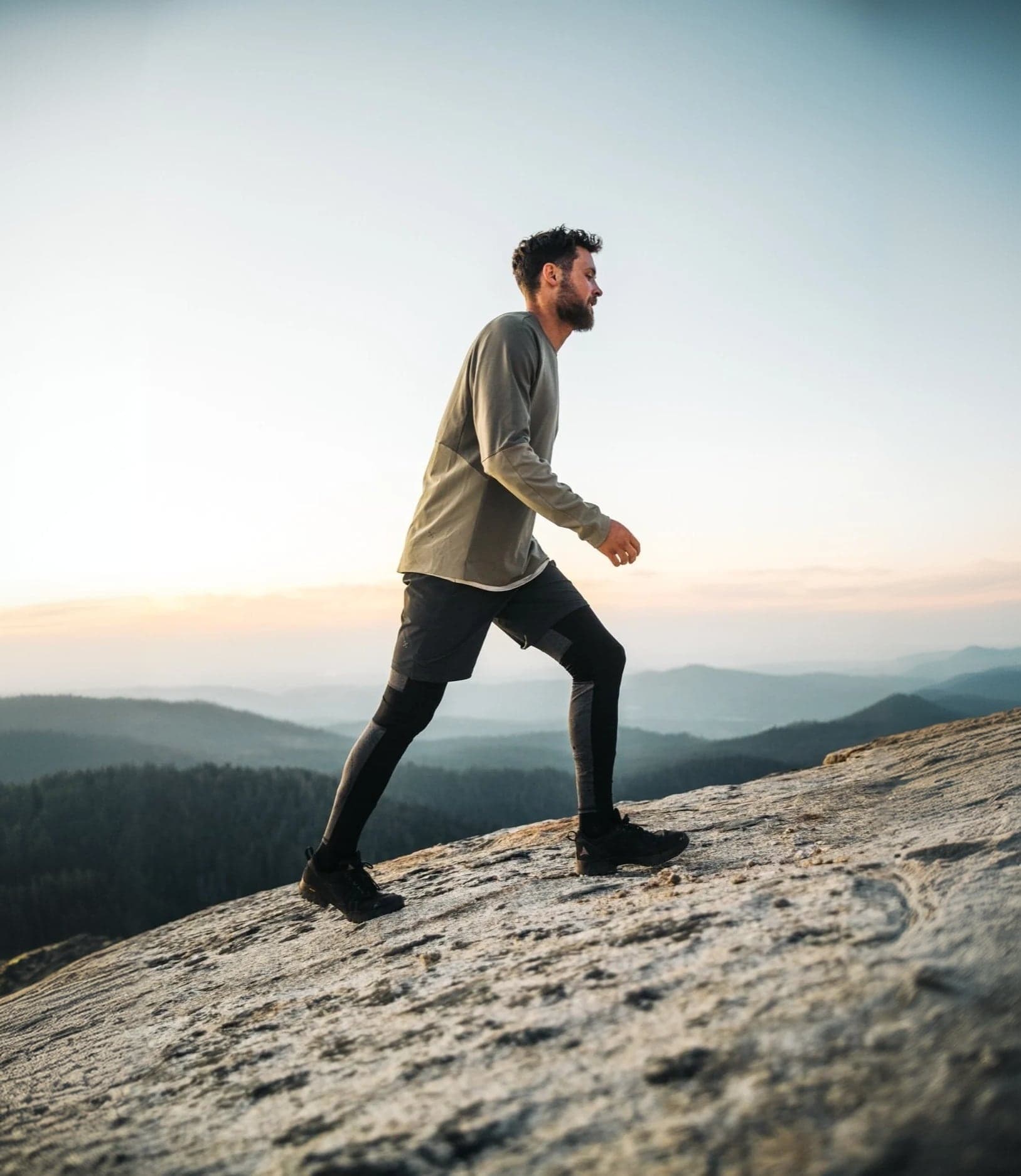 Hiker striding across a granite summit at sunrise
