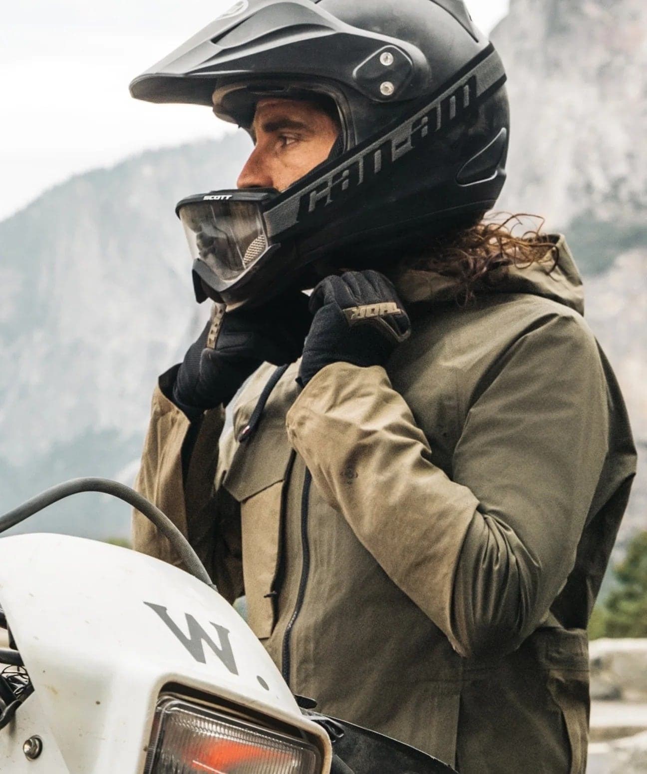 Rider in a helmet and waxed jacket beside a motorbike